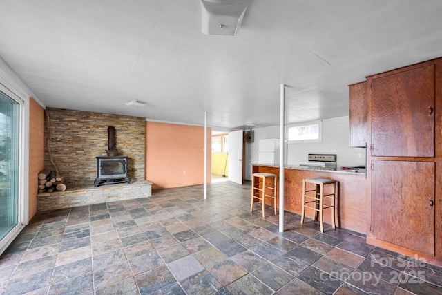 kitchen with brown cabinetry, a breakfast bar, open floor plan, a wood stove, and stone finish flooring