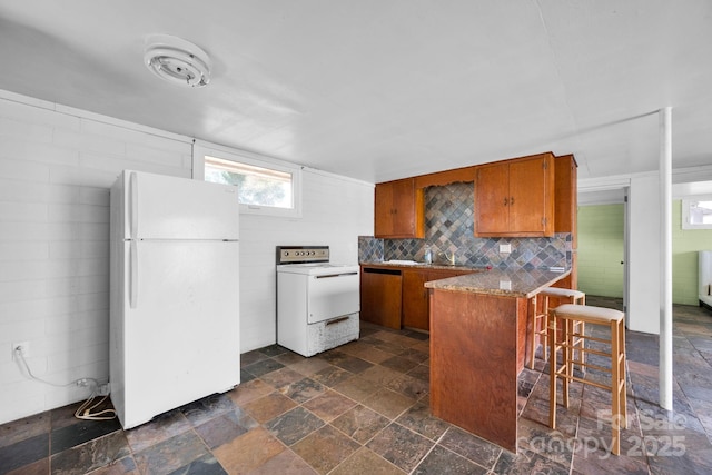 kitchen featuring a breakfast bar, brown cabinets, electric range oven, freestanding refrigerator, and a peninsula