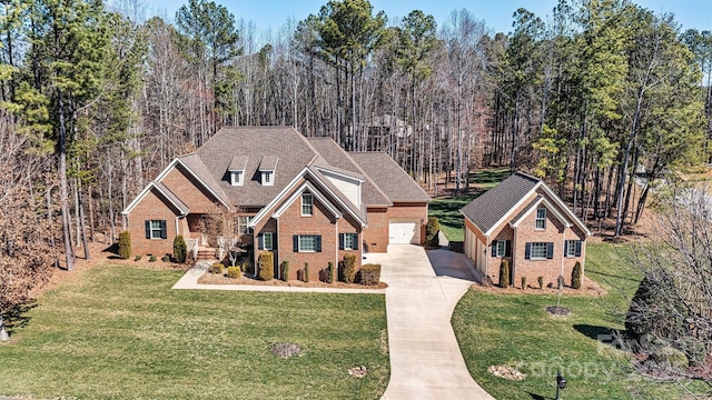 traditional-style house featuring brick siding, concrete driveway, a front yard, a wooded view, and a garage