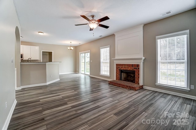 unfurnished living room with visible vents, ceiling fan with notable chandelier, a sink, dark wood finished floors, and a fireplace