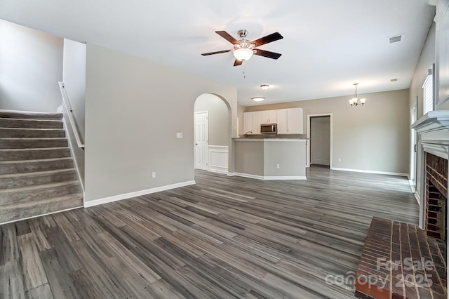 unfurnished living room featuring stairs, a brick fireplace, dark wood finished floors, and visible vents