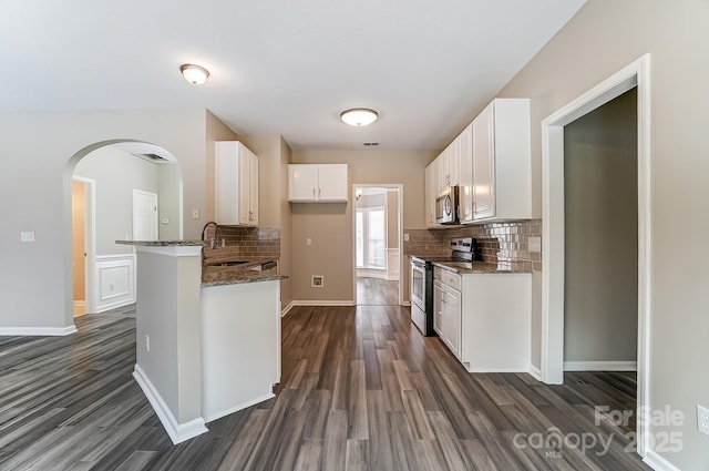 kitchen featuring dark stone counters, arched walkways, stainless steel appliances, dark wood-type flooring, and white cabinetry