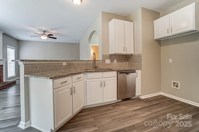 kitchen with a peninsula, a sink, white cabinets, stainless steel dishwasher, and tasteful backsplash