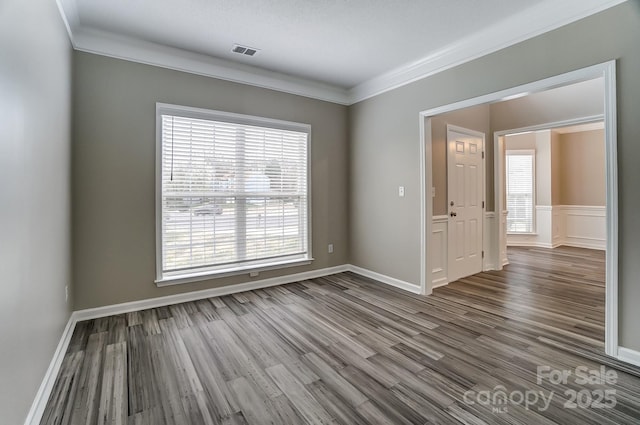 spare room with crown molding, wood finished floors, visible vents, and baseboards