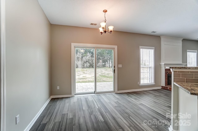 unfurnished dining area featuring visible vents, a brick fireplace, baseboards, and wood finished floors