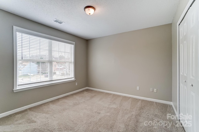 carpeted spare room featuring baseboards, visible vents, and a textured ceiling