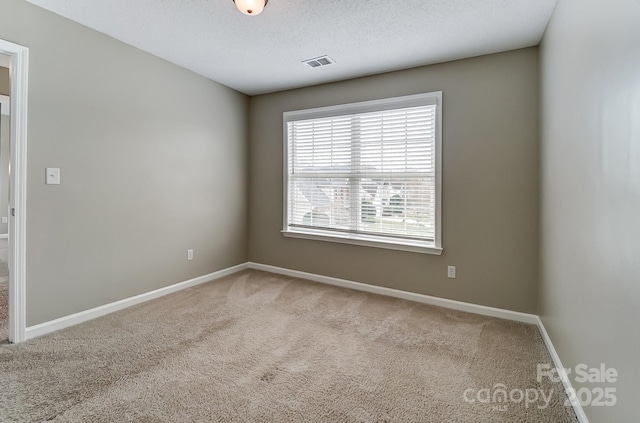 spare room featuring baseboards, visible vents, carpet floors, and a textured ceiling