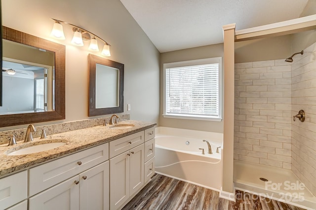 bathroom with wood finished floors, tiled shower, double vanity, a sink, and a bath