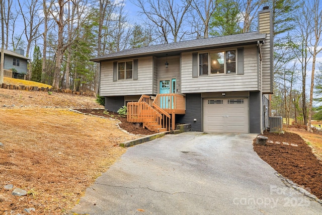 split foyer home with a garage, cooling unit, driveway, and a chimney