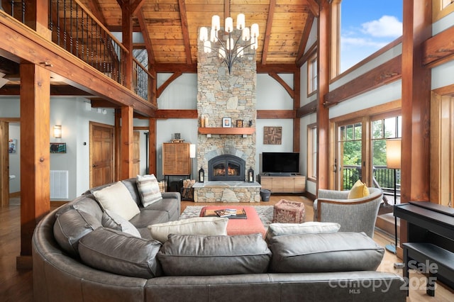 living area with beam ceiling, a notable chandelier, wood finished floors, a stone fireplace, and wood ceiling