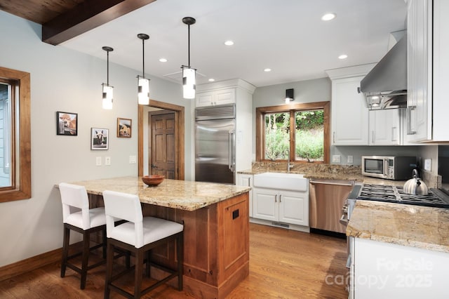 kitchen with a sink, wall chimney range hood, white cabinets, and stainless steel appliances