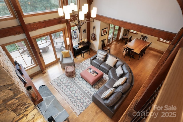 living area with a notable chandelier, a healthy amount of sunlight, a towering ceiling, and wood finished floors