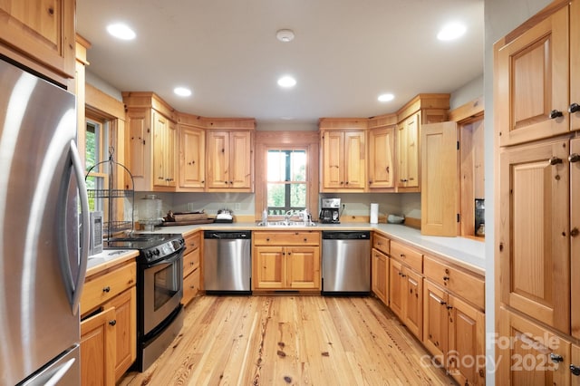 kitchen with light wood finished floors, light brown cabinetry, a sink, stainless steel appliances, and light countertops