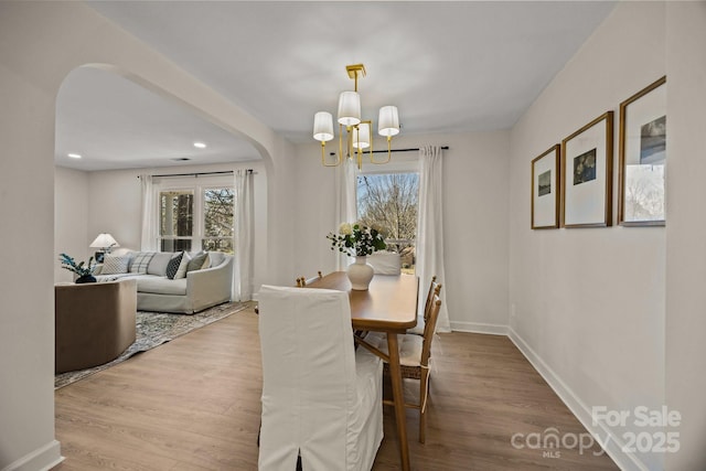 dining room with baseboards, arched walkways, wood finished floors, an inviting chandelier, and recessed lighting