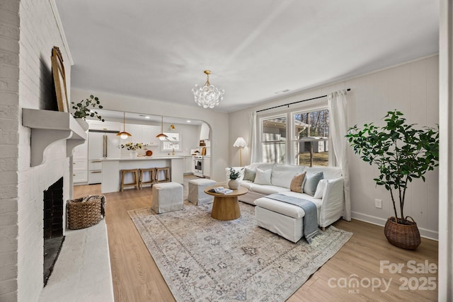 living room featuring arched walkways, a notable chandelier, a fireplace, baseboards, and light wood-type flooring