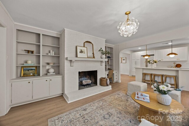 living area with light wood-style floors, arched walkways, a brick fireplace, and a notable chandelier