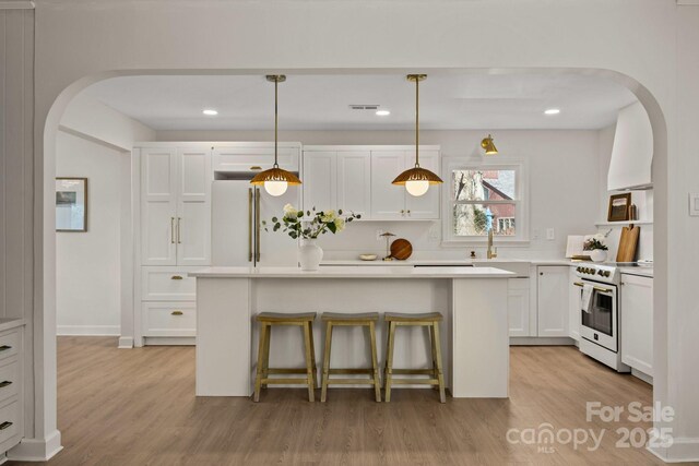 kitchen featuring white appliances, light wood-style flooring, arched walkways, and white cabinets