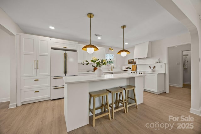 kitchen featuring arched walkways, white cabinetry, light countertops, white refrigerator, and custom range hood