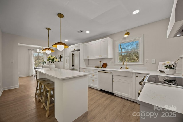 kitchen featuring visible vents, dishwasher, a breakfast bar area, high end fridge, and a sink