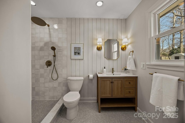 bathroom with baseboards, toilet, tile patterned flooring, a tile shower, and vanity