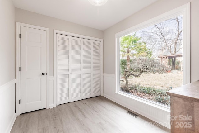 unfurnished bedroom featuring wainscoting, a closet, visible vents, and light wood-type flooring