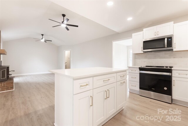 kitchen featuring ceiling fan, a wood stove, stainless steel appliances, and light wood-style flooring