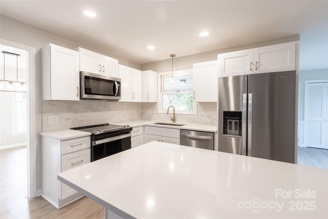 kitchen with appliances with stainless steel finishes, tasteful backsplash, a sink, and light wood-type flooring