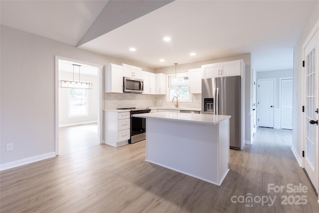 kitchen featuring light wood-style floors, white cabinetry, light countertops, a kitchen island, and appliances with stainless steel finishes