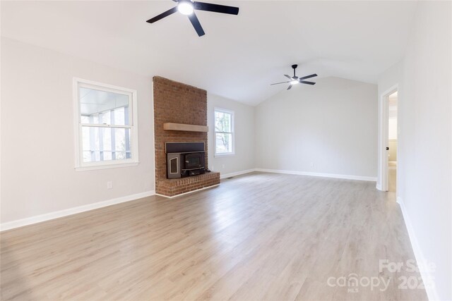 unfurnished living room with vaulted ceiling, light wood-type flooring, a wood stove, and ceiling fan