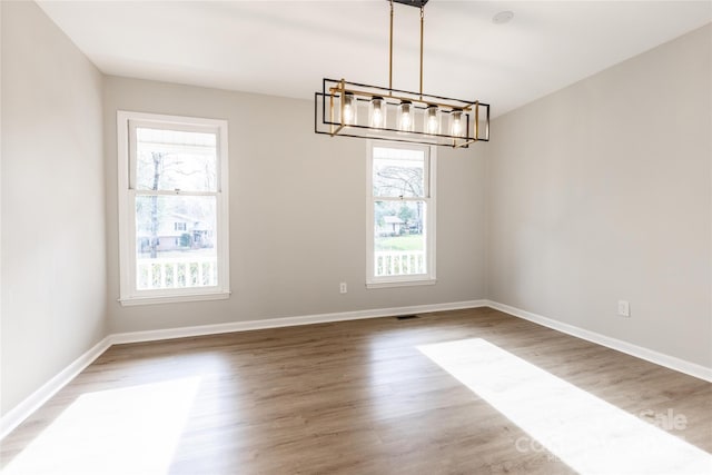 unfurnished dining area with wood finished floors, a healthy amount of sunlight, and a notable chandelier