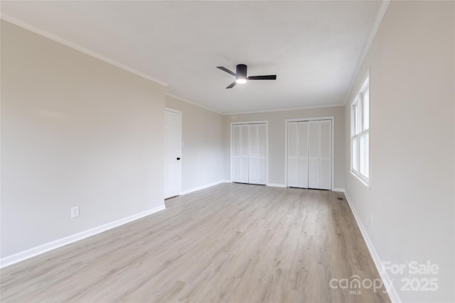 unfurnished bedroom featuring light wood-style flooring, multiple closets, crown molding, and baseboards