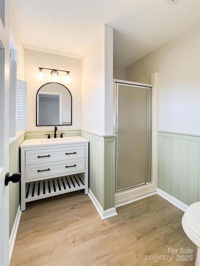 full bath featuring wainscoting, wood finished floors, and a stall shower