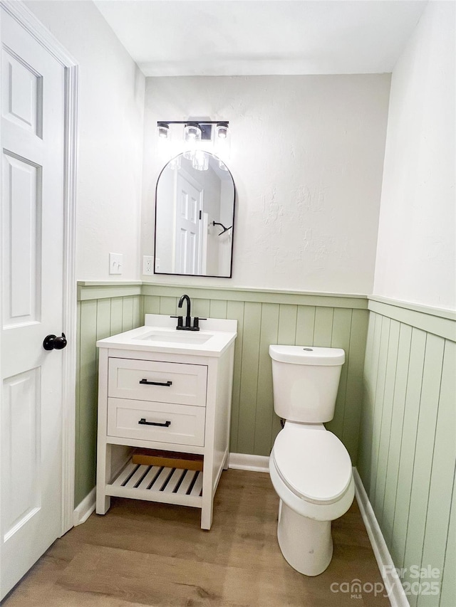 half bathroom with wainscoting, toilet, vanity, and wood finished floors