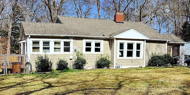 rear view of house featuring roof with shingles, a chimney, and a yard