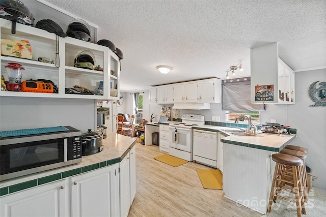 kitchen with a peninsula, white appliances, a textured ceiling, under cabinet range hood, and white cabinets