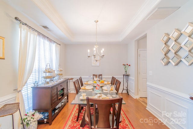 dining space featuring a tray ceiling, light wood-style floors, a chandelier, and wainscoting