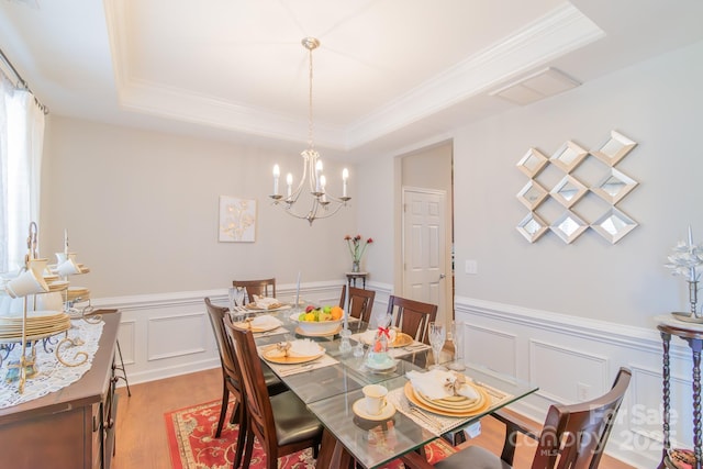 dining room featuring visible vents, light wood-type flooring, a tray ceiling, ornamental molding, and an inviting chandelier