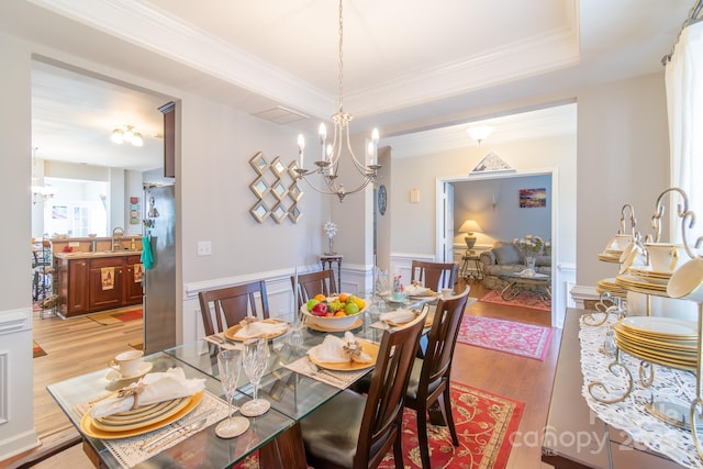 dining area with a wainscoted wall, light wood-style flooring, a tray ceiling, an inviting chandelier, and crown molding