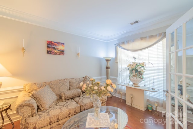 living area with visible vents, wood finished floors, and ornamental molding