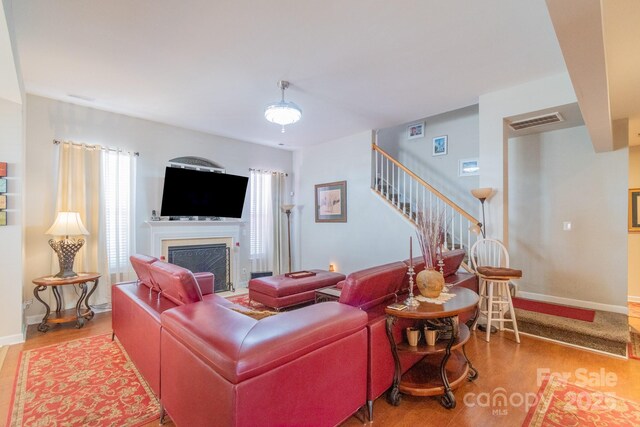 living area featuring visible vents, a fireplace, light wood finished floors, baseboards, and stairs