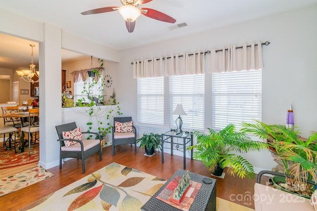 sitting room with visible vents, wood finished floors, and ceiling fan with notable chandelier