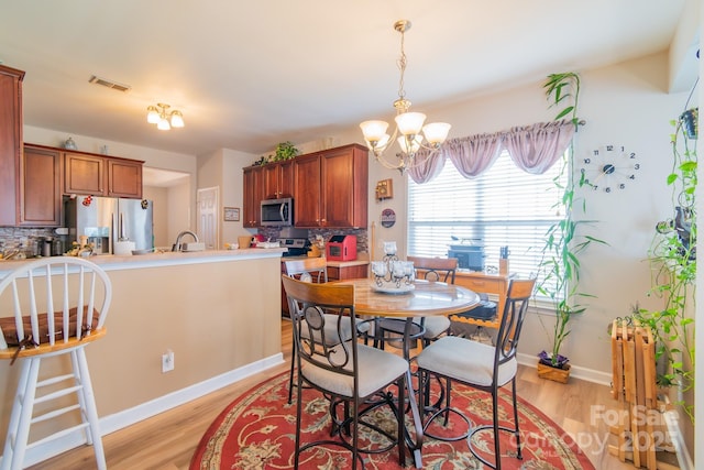 dining space with baseboards, light wood-style floors, visible vents, and a chandelier