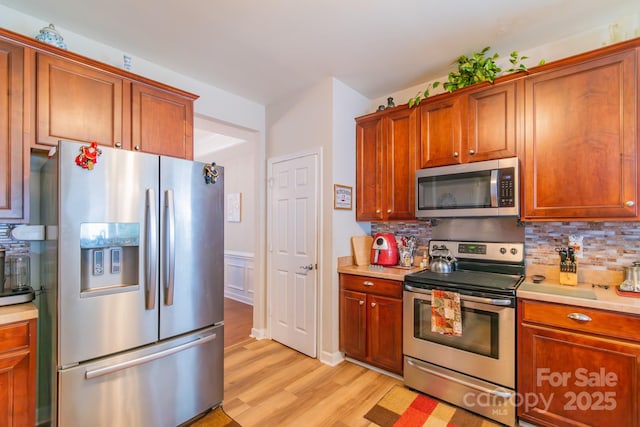 kitchen with light countertops, tasteful backsplash, light wood-type flooring, and appliances with stainless steel finishes