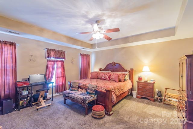 carpeted bedroom featuring a tray ceiling, visible vents, and a ceiling fan