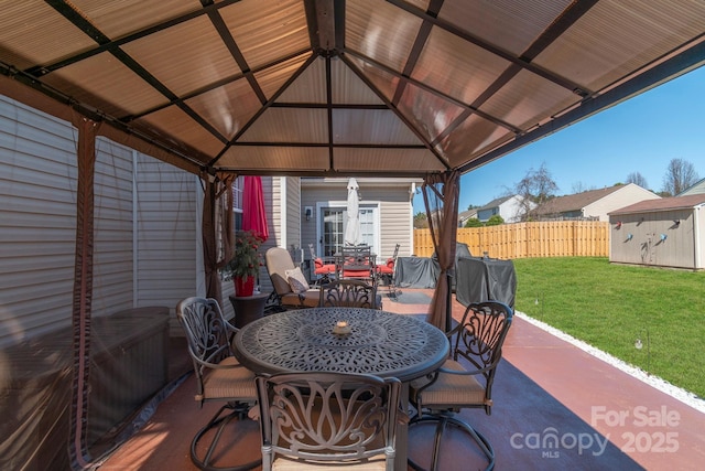 view of patio with an outbuilding, fence, a shed, outdoor dining area, and a gazebo