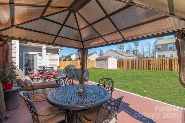 view of patio with a gazebo, a storage shed, outdoor dining area, a fenced backyard, and an outbuilding