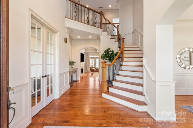 foyer entrance featuring arched walkways, light wood finished floors, crown molding, and a decorative wall