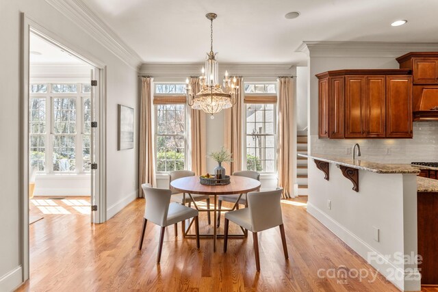 dining space featuring baseboards, ornamental molding, an inviting chandelier, and light wood-style floors