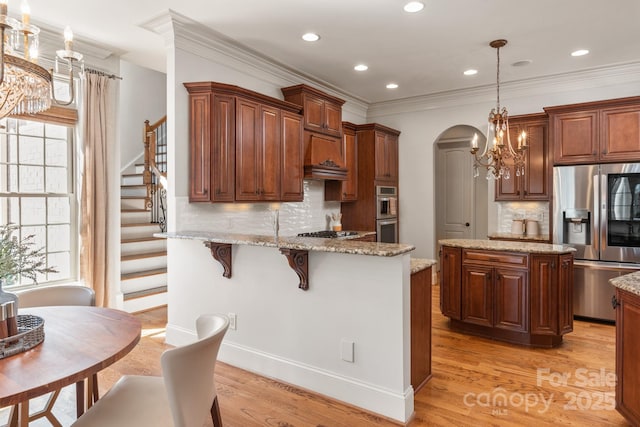 kitchen with arched walkways, light wood finished floors, stainless steel appliances, hanging light fixtures, and a kitchen island