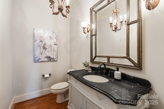 bathroom featuring a notable chandelier, toilet, vanity, wood finished floors, and baseboards